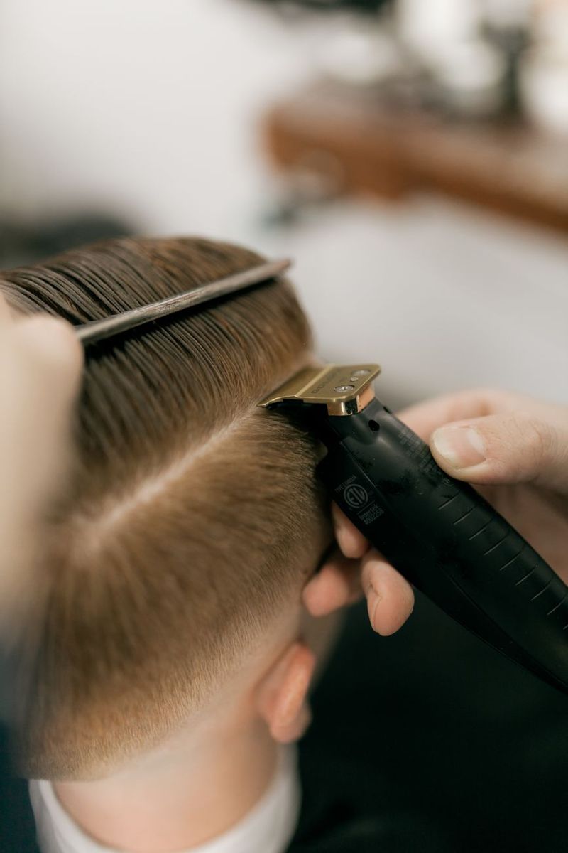 Barber using clippers and a comb to shape a close cut